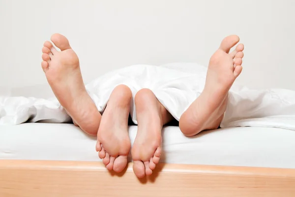 Feet of couple in bed.