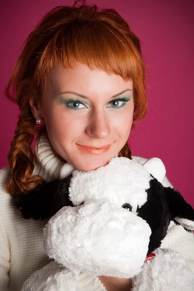 Portrait of a red-haired girl in a white sweater with a soft toy