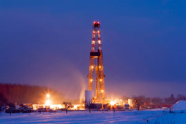 Oil well in the snowy landscape lit up at night.