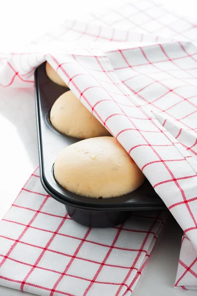 Yeast dough in a muffin pan with a white and red towel on white