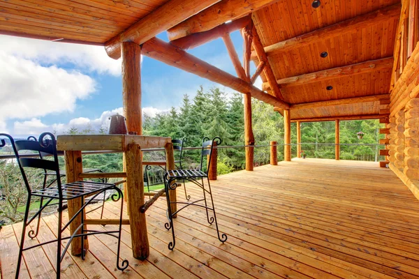 Porch of the log cabin with small table and forest view.