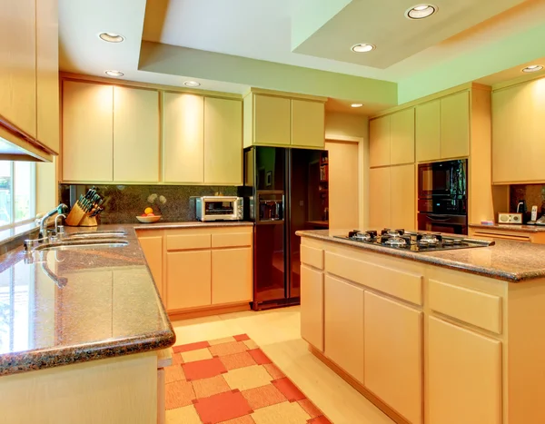 Large kitchen with honey wood and black appliances.