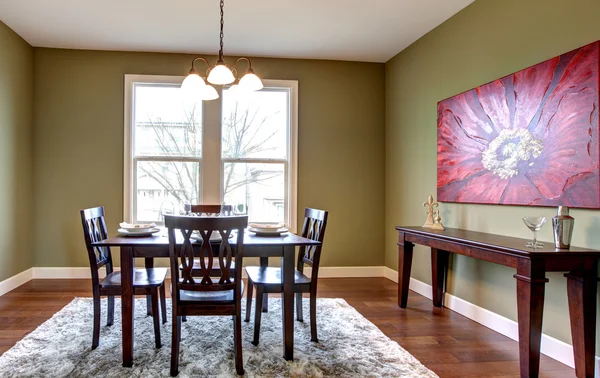 Dining room with green walls and red painting.