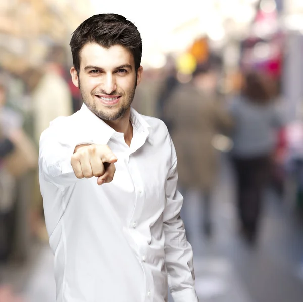 Portrait of a handsome young man pointing with finger at a crowd