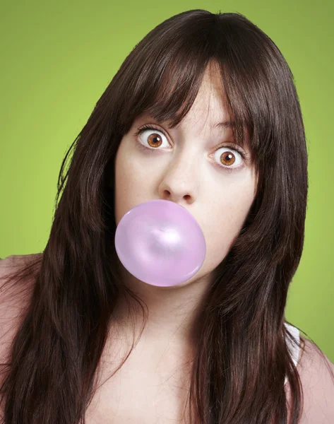 Young girl with a pink bubble of chewing gum against a green bac