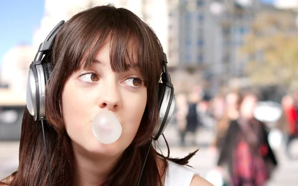 Portrait of young woman listening to music with bubble gum at cr