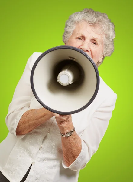 Portrait of senior woman screaming with megaphone over green bac