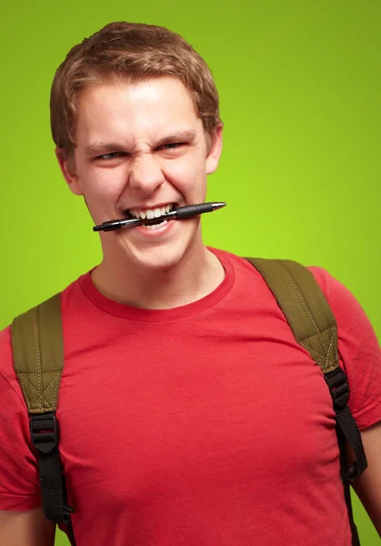 Portrait of angry young man biting pen over green background
