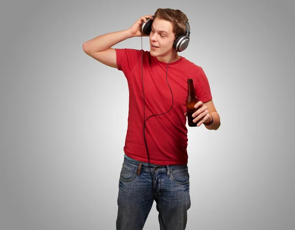 Portrait of young man listening music and holding beer on grey b