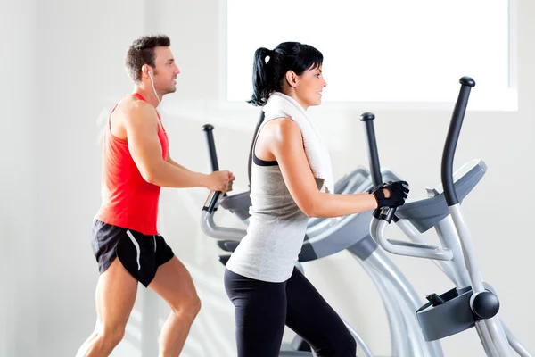 Man and woman with elliptical cross trainer at gym