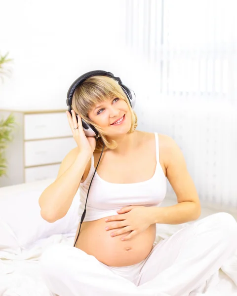 Happy pregnant woman listening music in headphones
