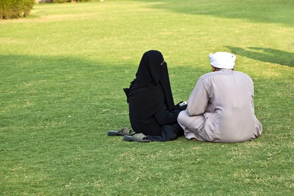 Islamic woman in burka sitting on the green with her husband
