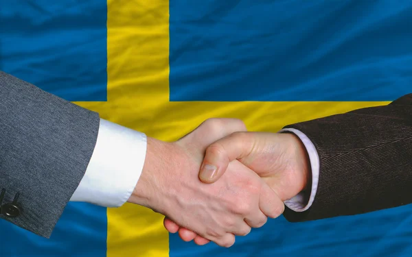 Businessmen handshake after good deal in front of sweden flag