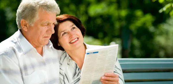 Happy senior couple reading outdoors