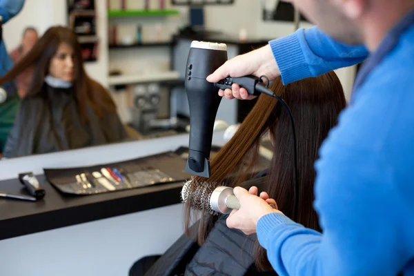 Hairdresser drying woman\'s hair using hair dryer and round brush