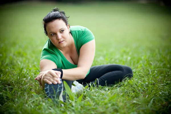 Plus sized woman stretching in a park. Shallow DOF.