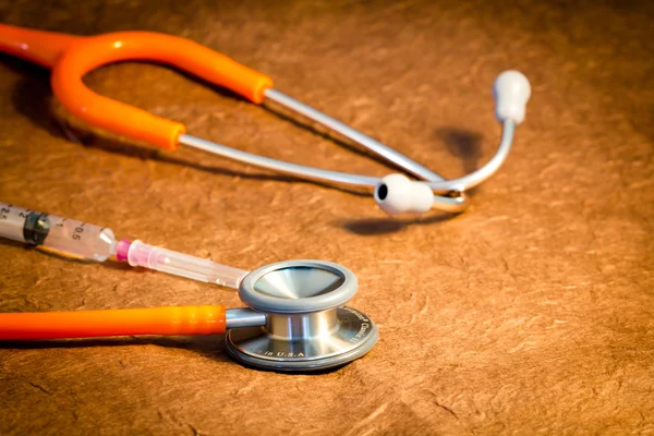 Medical stethoscope and syringe over brown background