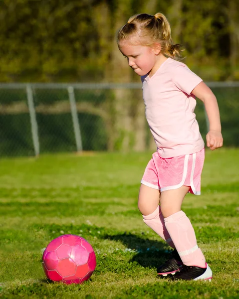 Cute young girl in pink playing soccer on field