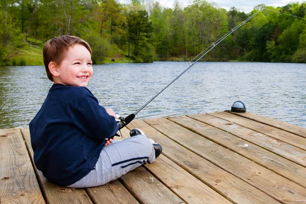 Boy fishing from dock on lake.