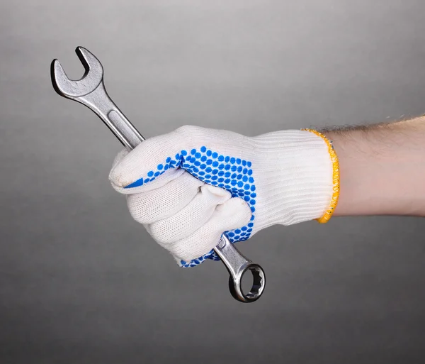 Wrench in hand with protection glove on grey background