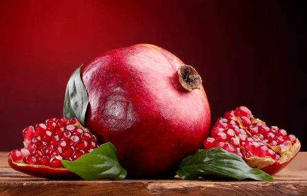 Ripe pomegranate fruit with leaves on wooden table on red background