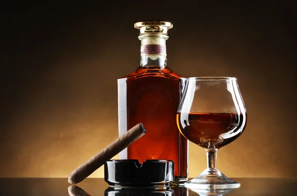 Bottle and glass of brandy and cigar on brown background