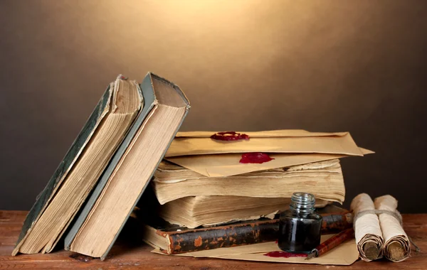 Old books, scrolls, ink pen and inkwell on wooden table on brown background