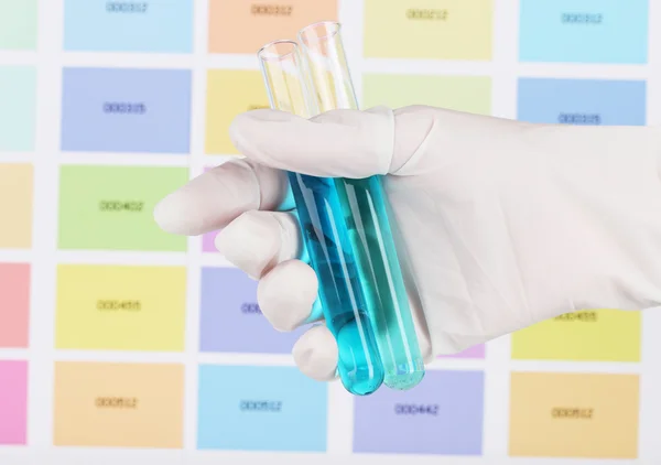 Two tubes with blue and dark blue liquid in hand on color samples background
