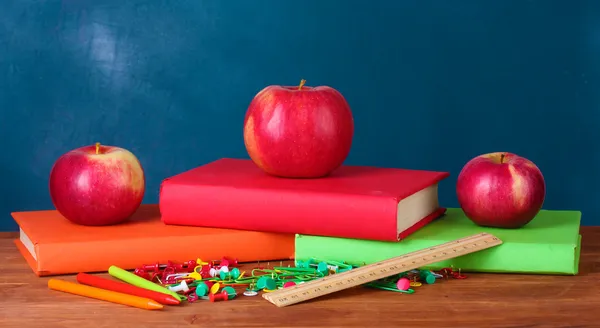 Composition of books, stationery and an apples on the teachers desk in the background of the blackboard