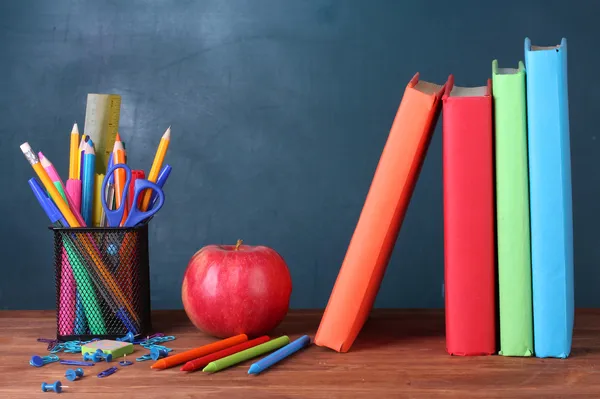 Composition of books, stationery and an apple on the teachers desk in the background of the blackboard