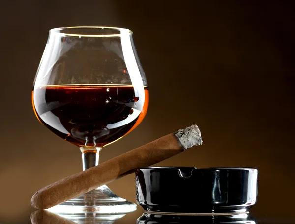 Glass of brandy and cigar on brown background