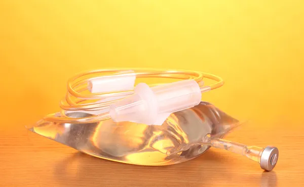 Bag of intravenous antibiotics and plastic infusion set on wooden table on yellow background