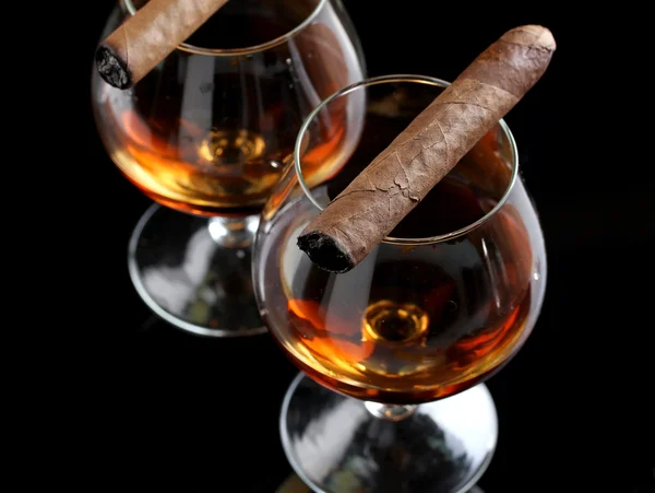 Two glasses of brandy and cigars on black background