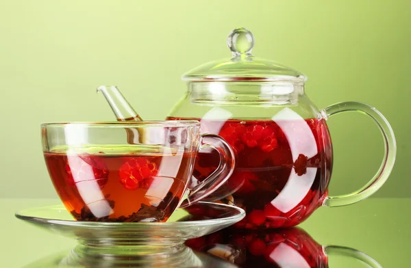 Black fruit raspberry tea in glass teapot and cup on green background
