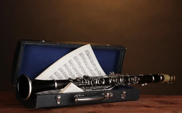Old clarinet and notebook with notes in case on wooden table on brown backg
