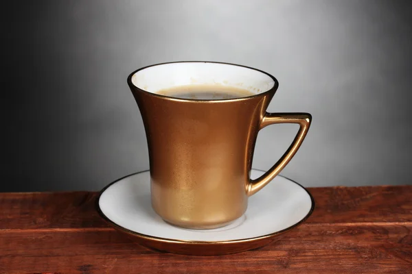 Golden cup of coffee on wooden table on gray background