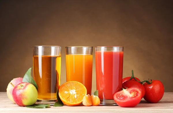 Different juices and fruits on wooden table on brown background