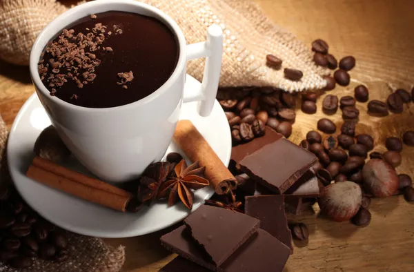 Cup of hot chocolate, cinnamon sticks, nuts and chocolate on wooden table