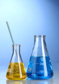 Two flasks with yellow and blue liquid with reflection on blue background