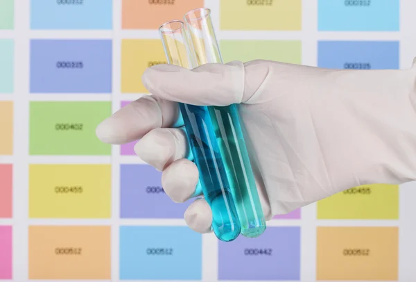 Two tubes with blue and dark blue liquid in hand on color samples backgroun