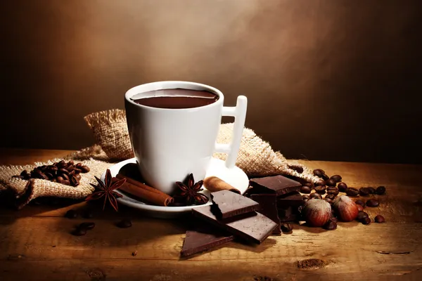 Cup of hot chocolate, cinnamon sticks, nuts and chocolate on wooden table o