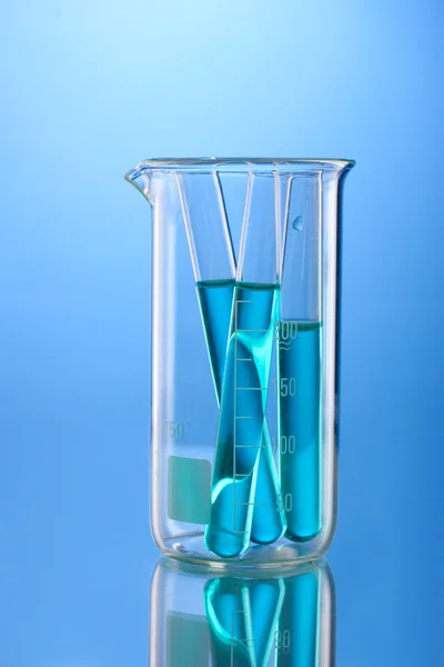 Laboratory tubes with blue liquid in measuring beaker with reflection on bl