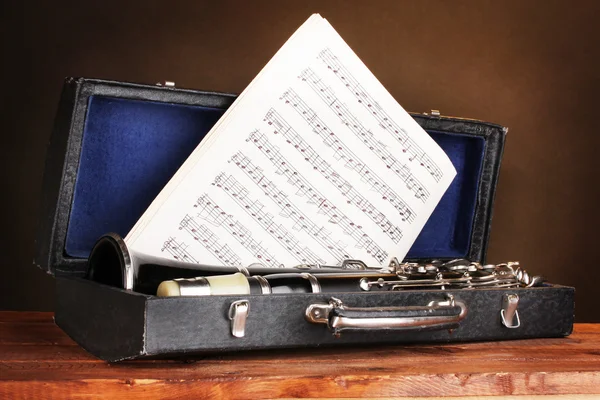 Old clarinet and notebook with notes in case on wooden table on brown backg