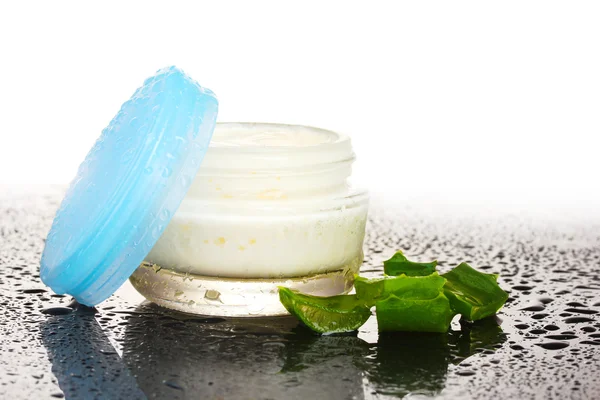 Opened glass jar of cream and aloe on black and white background with water
