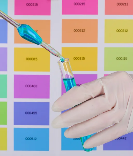 Test-tube with blue liquid and pipette in scientist's hands on color s