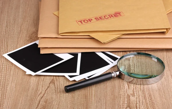 Envelopes with top secret stamp with photo papers and magnifying glass on w