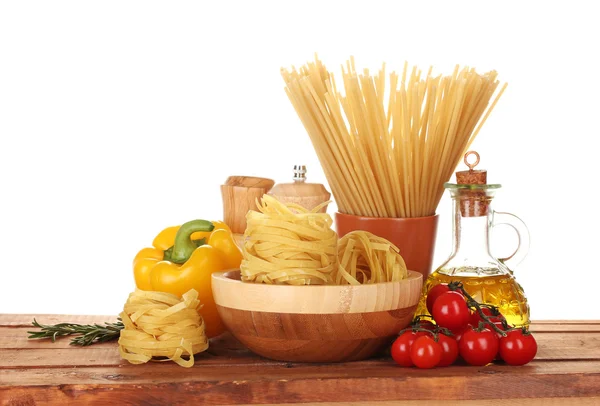 Spaghetti, noodles in bowl, jar of oil and vegetables on wooden table isola