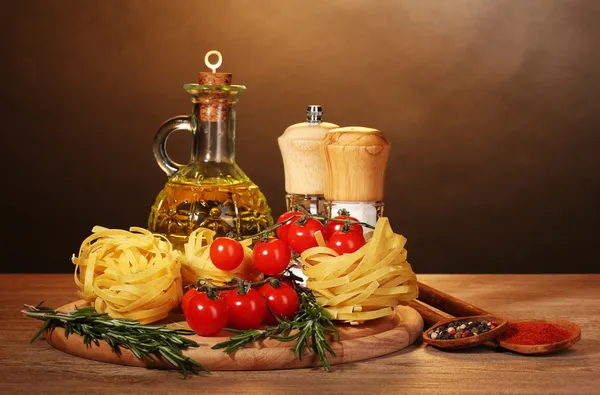 Noodles in bowl, jar of oil, spices and vegetables on wooden table on brown