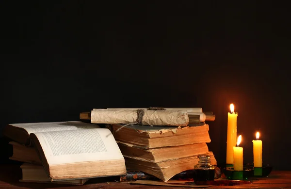 Old books, scrolls, ink pen inkwell and candles on wooden table on brown ba