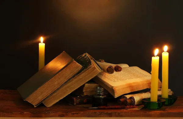 Old books, scrolls, ink pen inkwell and candles on wooden table on brown ba